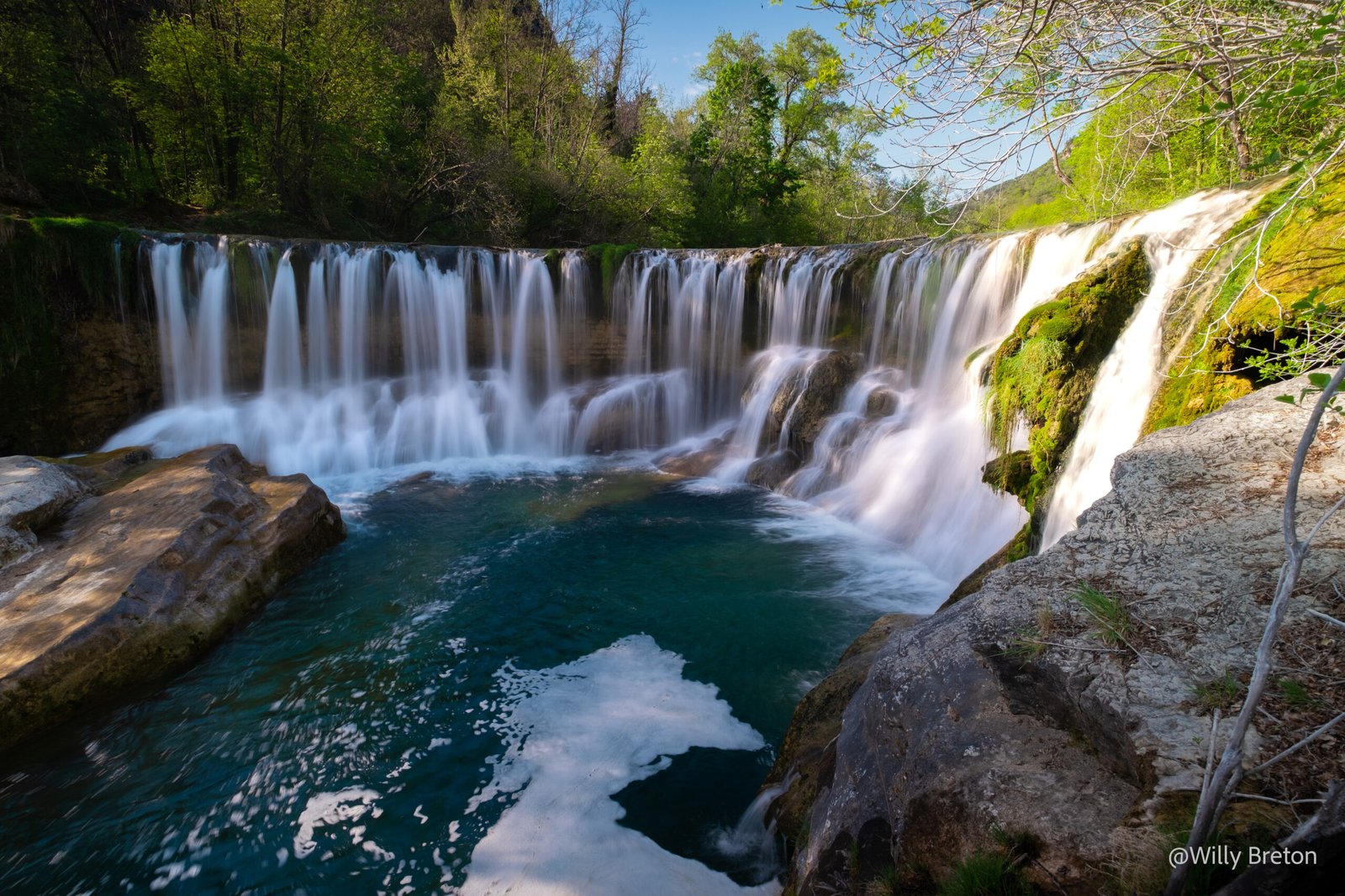 Cascade cristalline entourée de verdure printanière, représentant la vitalité et la beauté naturelle.