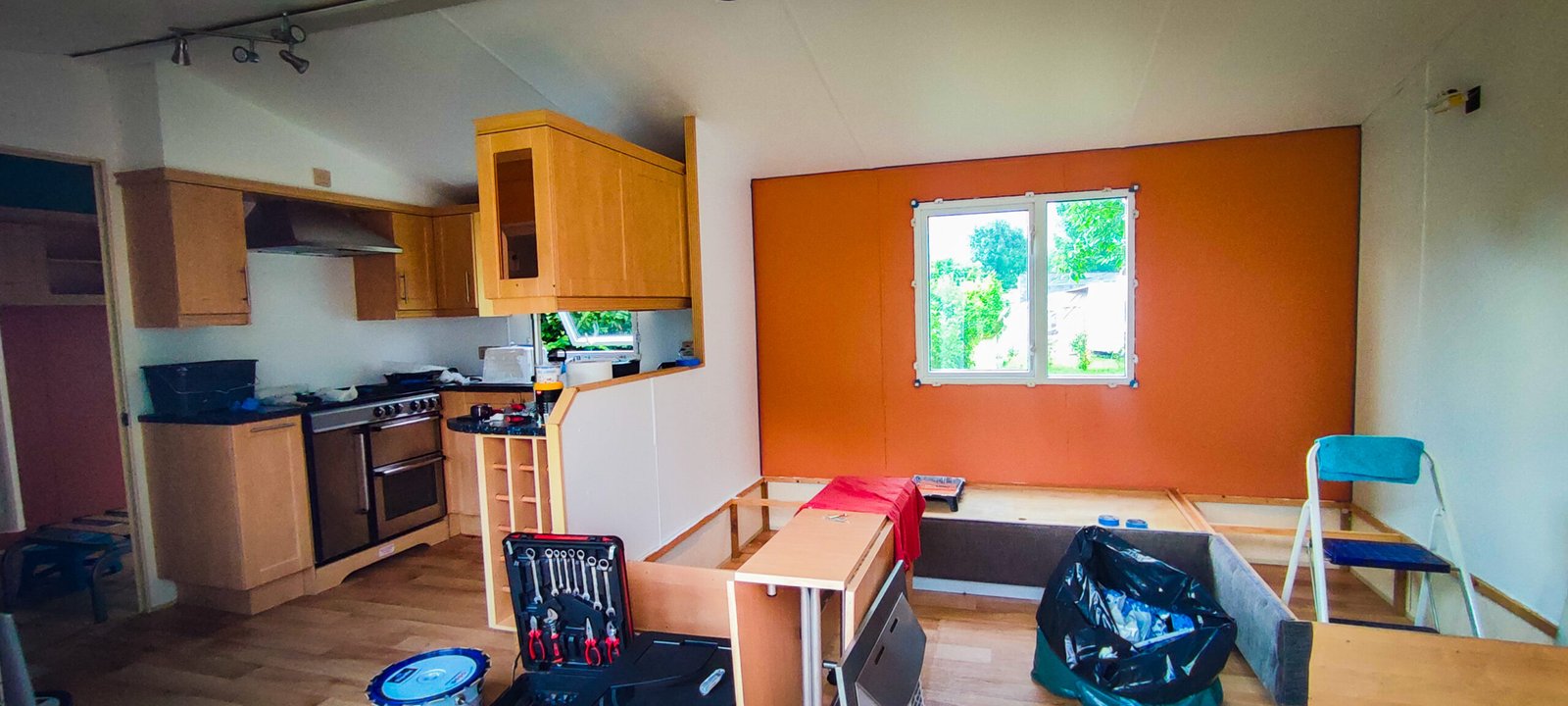 Travaux d'aménagement intérieur de mobile home dans une pièce avec cuisine équipée en bois, murs colorés et outils de bricolage au sol.