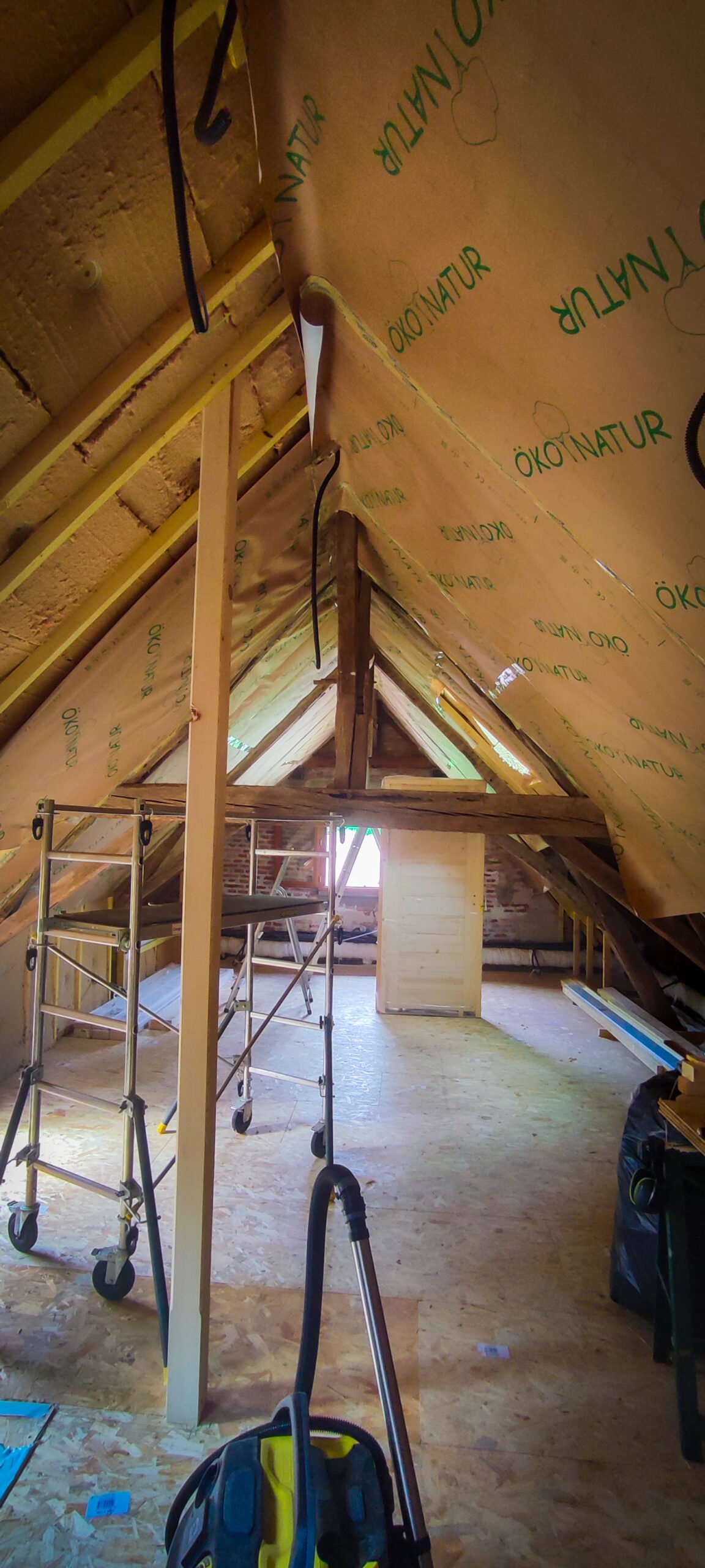 Grenier en rénovation avec isolation fibre de bois et pare vapeur Öko Natur, poutres apparentes et échafaudage mobile pour les travaux.