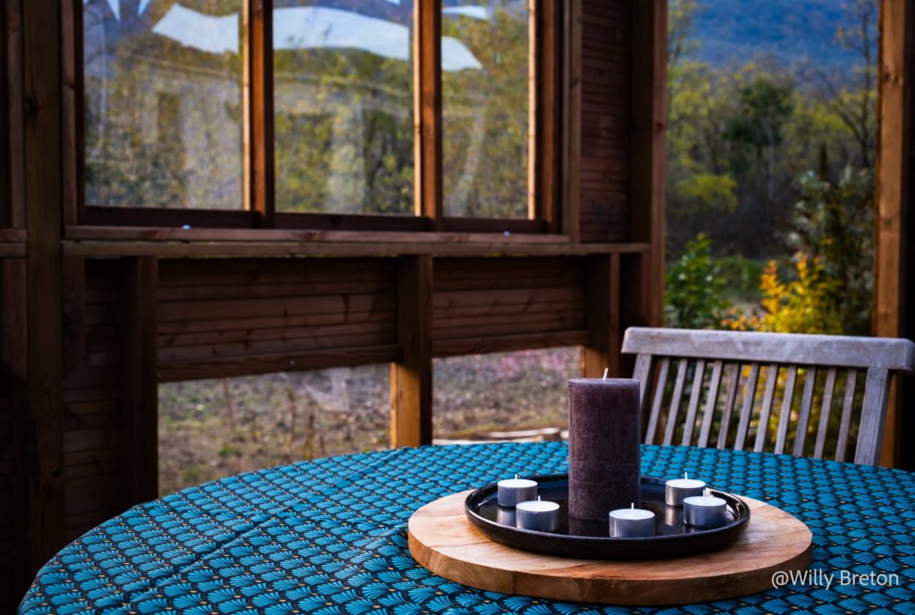 Table décorée avec une bougie et des photophores, située dans une véranda en bois avec vue sur la nature environnante.